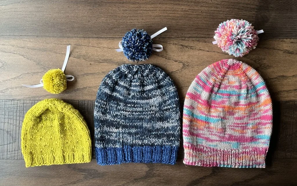 Three blocked, knitted hats with matching pompoms.