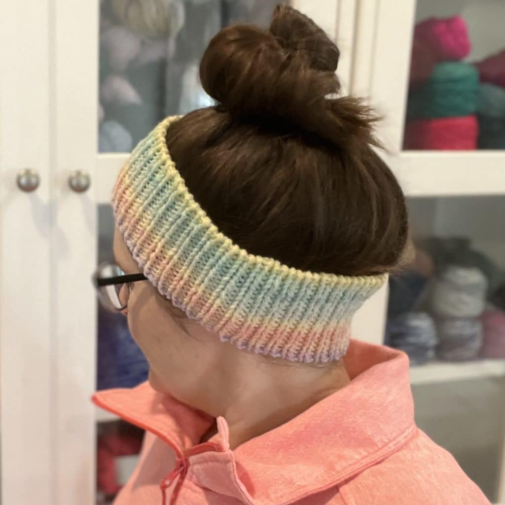 Endless Love Spell Ear Warmer Pattern Woman with dark brown hair in a messy bun wearing a ribbed ear warmer with gradient colors.