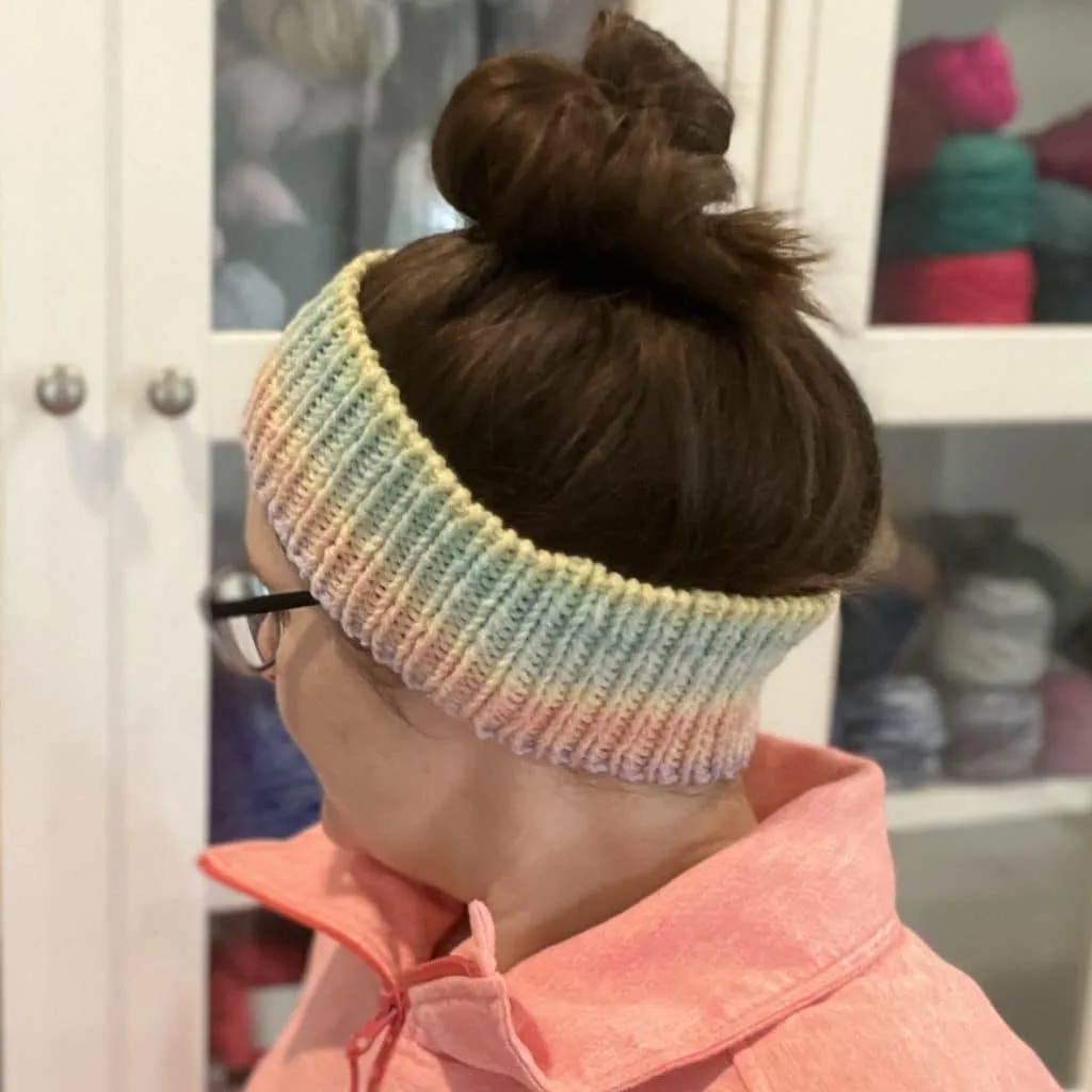 Endless Love Spell Ear Warmer Pattern Woman with dark brown hair in a messy bun wearing a ribbed ear warmer with gradient colors.