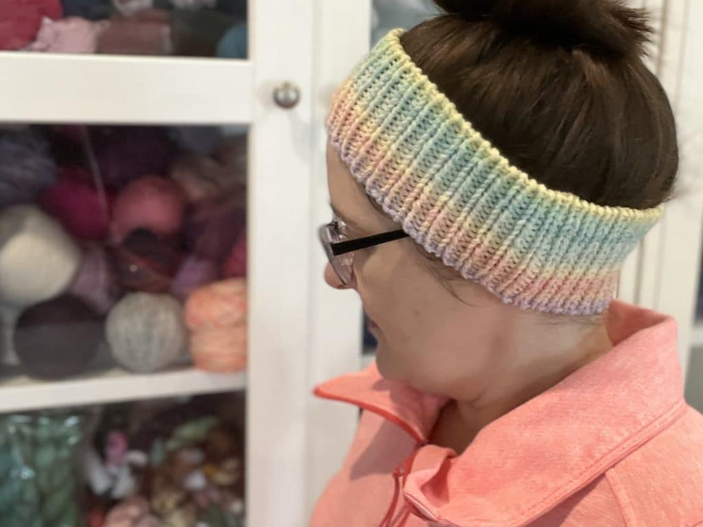 Endless Love Spell Ear Warmer Pattern Woman with dark brown hair in a messy bun wearing a ribbed ear warmer with gradient colors.